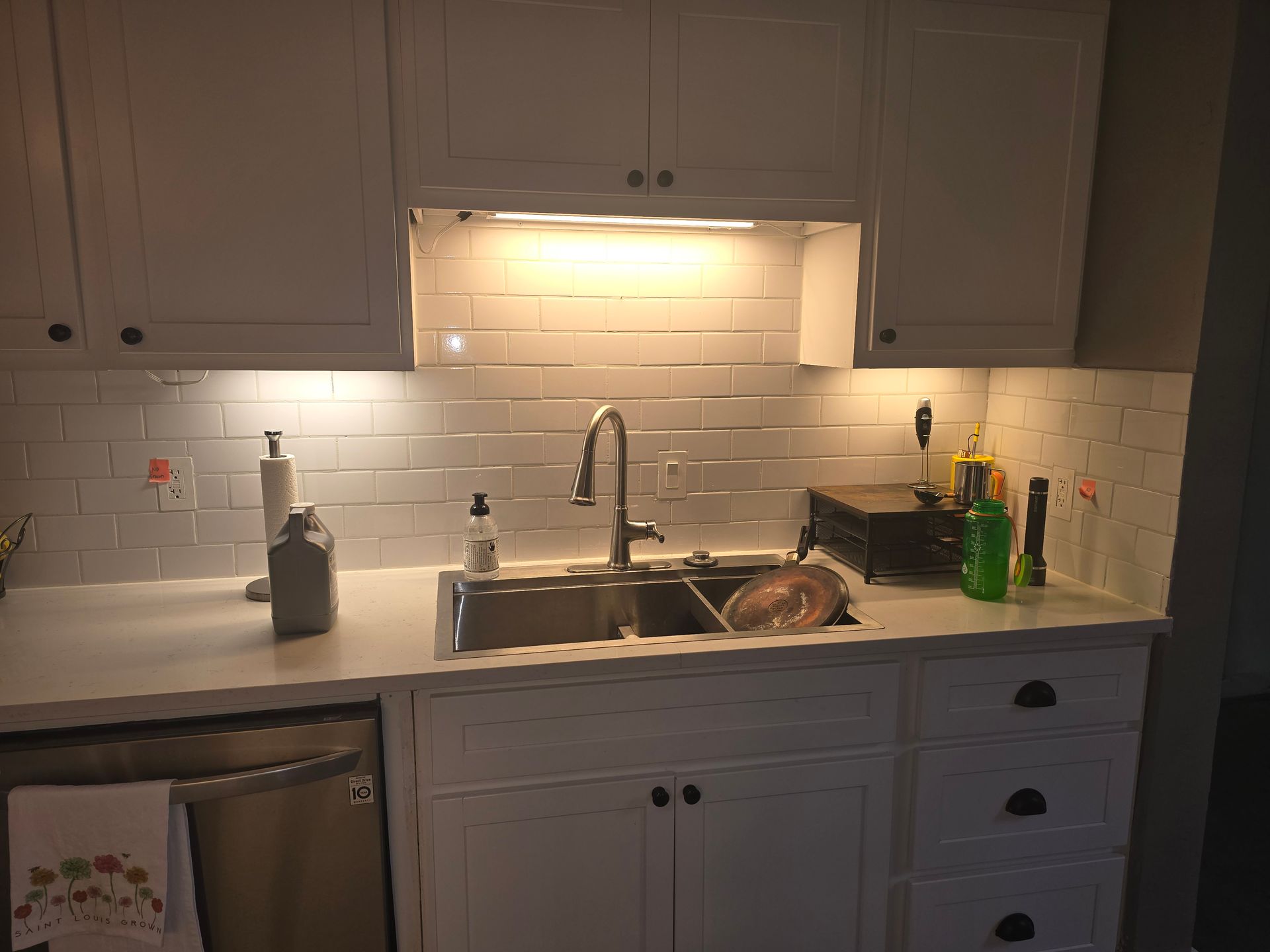 A kitchen with a sink , dishwasher , and white cabinets.