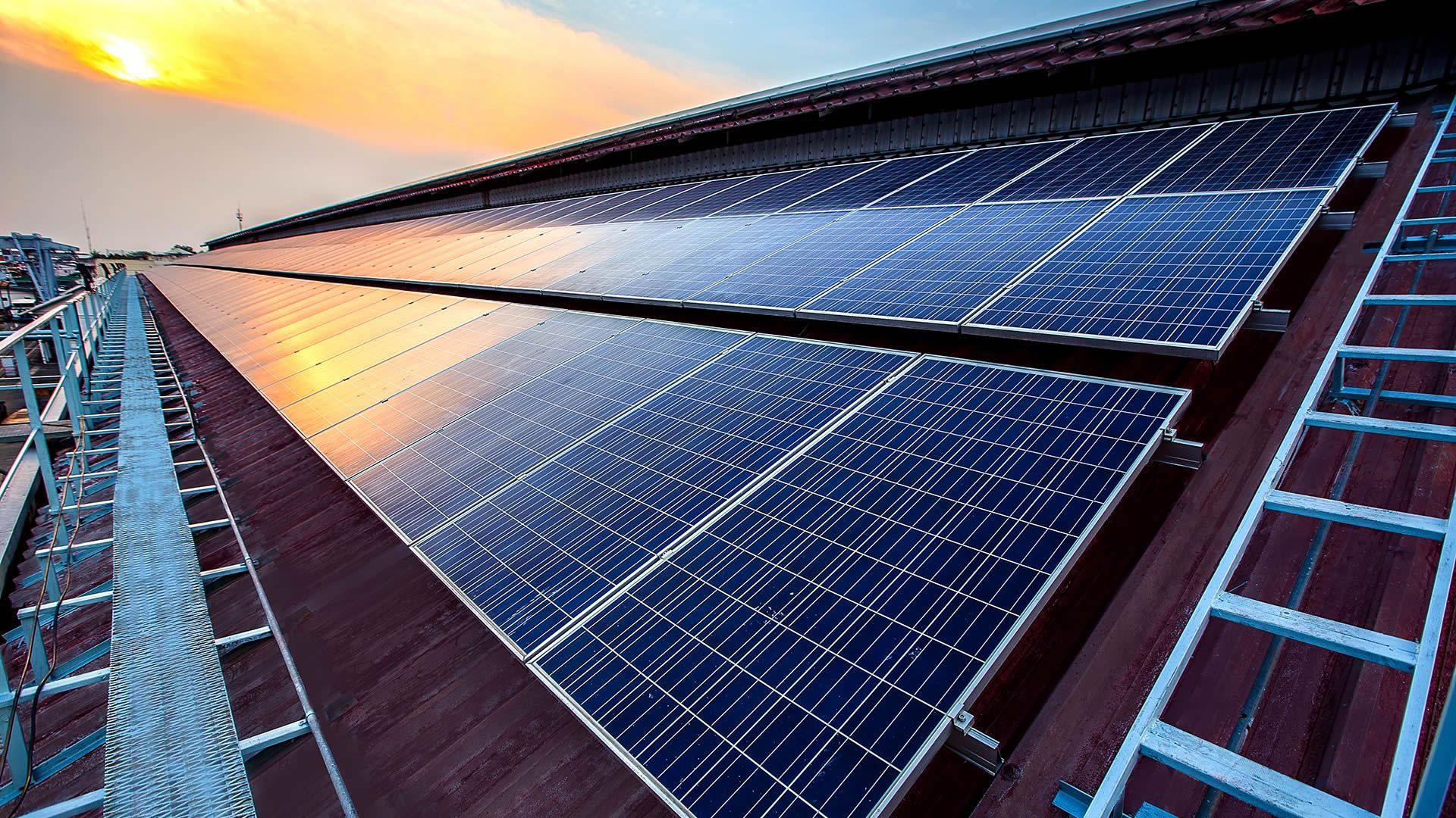 A man is sitting on the roof of a building looking at solar panels.