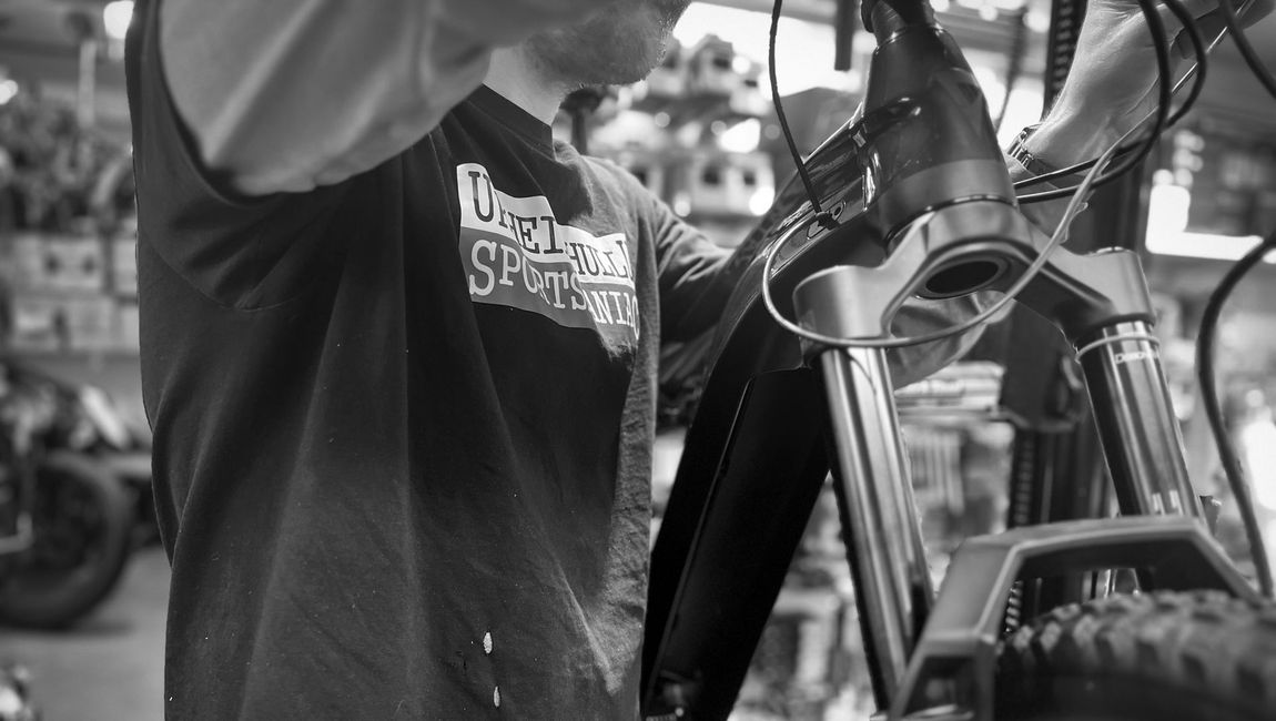 A man is working on a bicycle in a black and white photo.