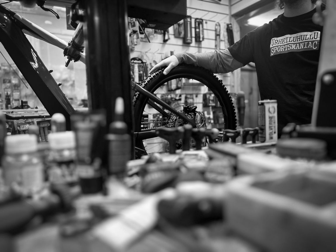 A man is working on a bicycle wheel in a black and white photo.