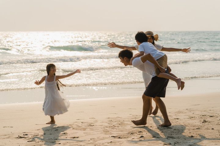 A man is carrying two children on his shoulders on the beach.