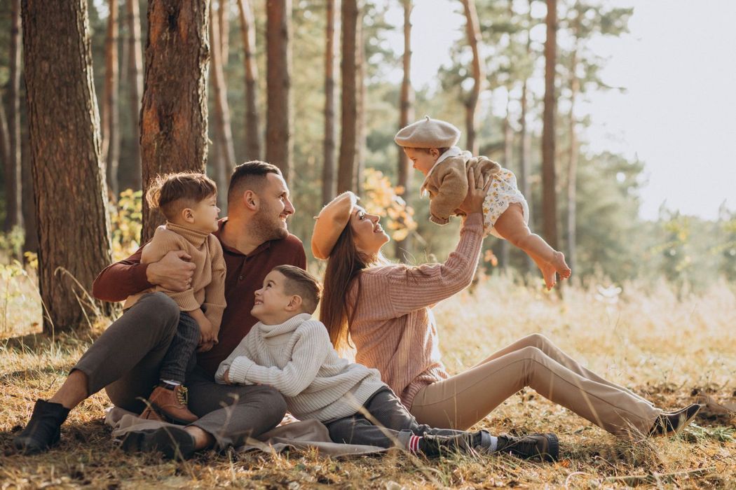 A family is sitting on the ground in the woods.