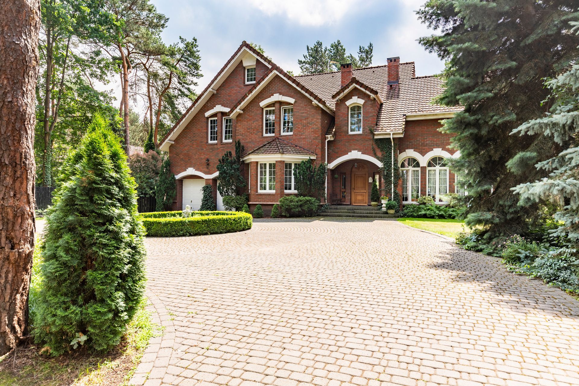 A large brick house with a brick driveway and trees in front of it.