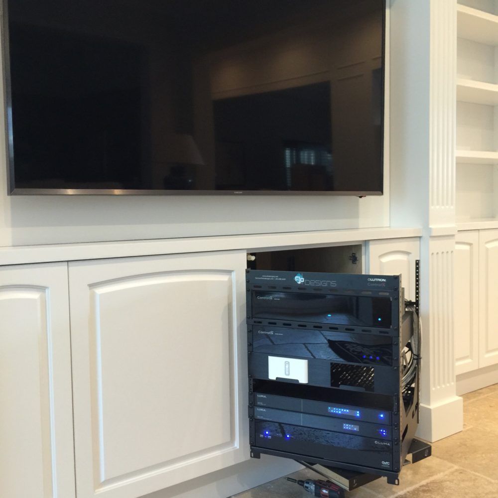 A large TV above a cabinet with audio/video equipment rack pulled out for access in a white built-in unit.