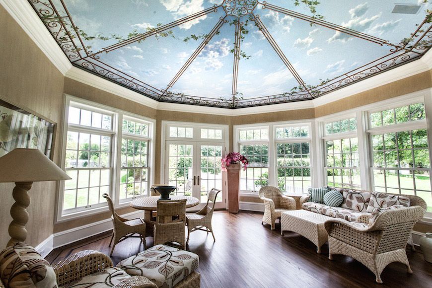 Sunroom with painted sky ceiling, wicker furniture, windows, and table with chairs.