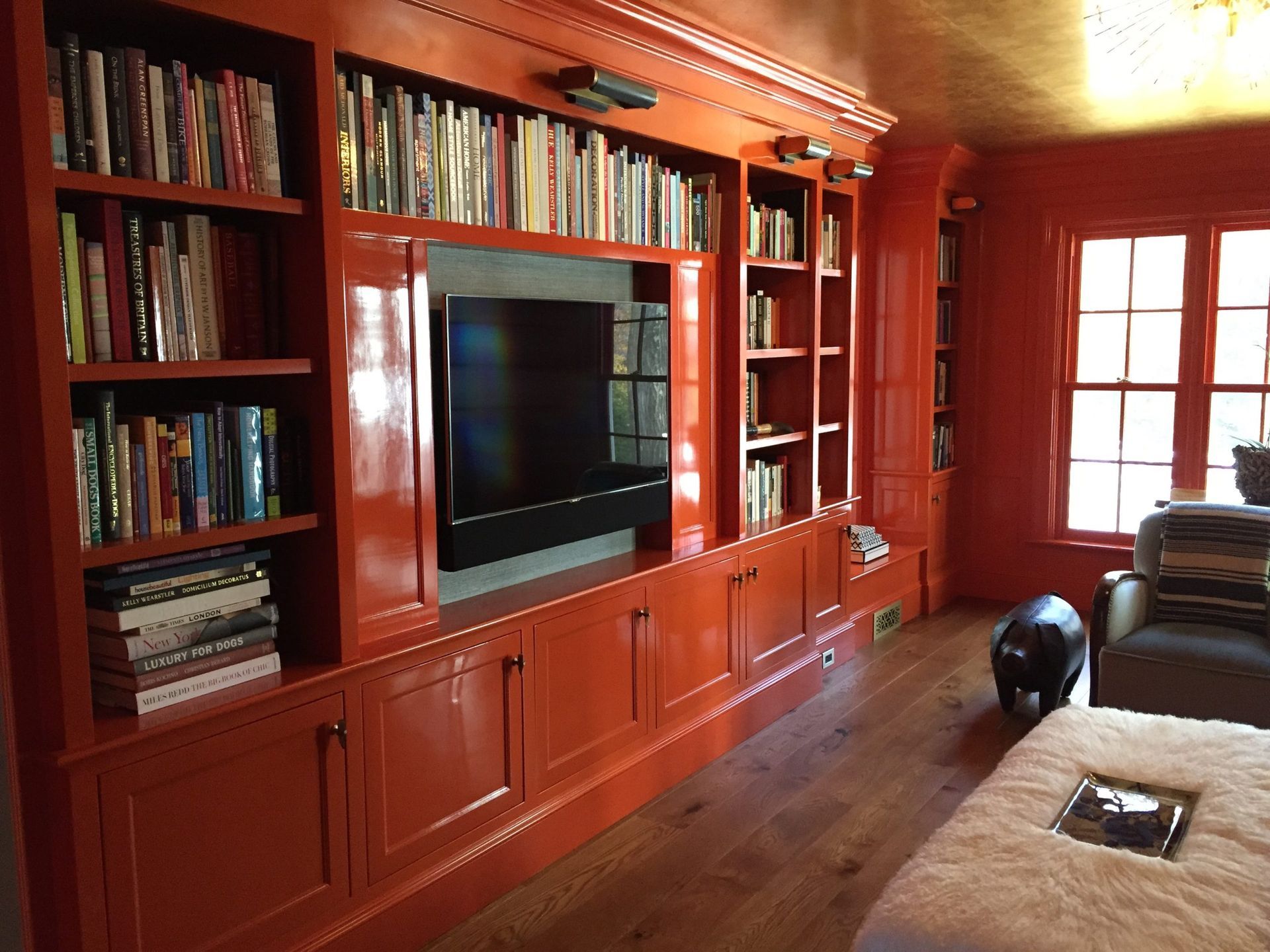 Bright orange built-in bookcase with TV, filled with books, in a room with wood floor and window.