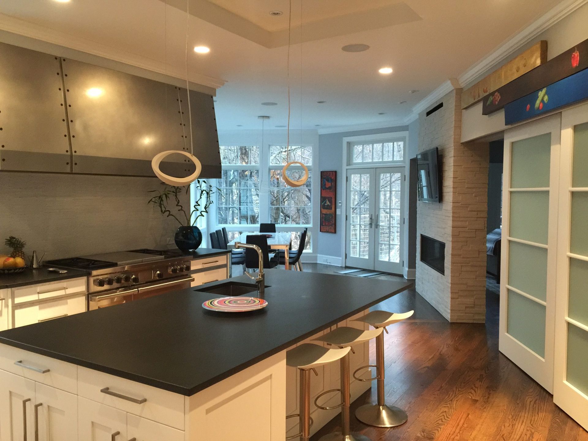 Modern kitchen with island, stainless steel range hood, and dining area with snowy view.