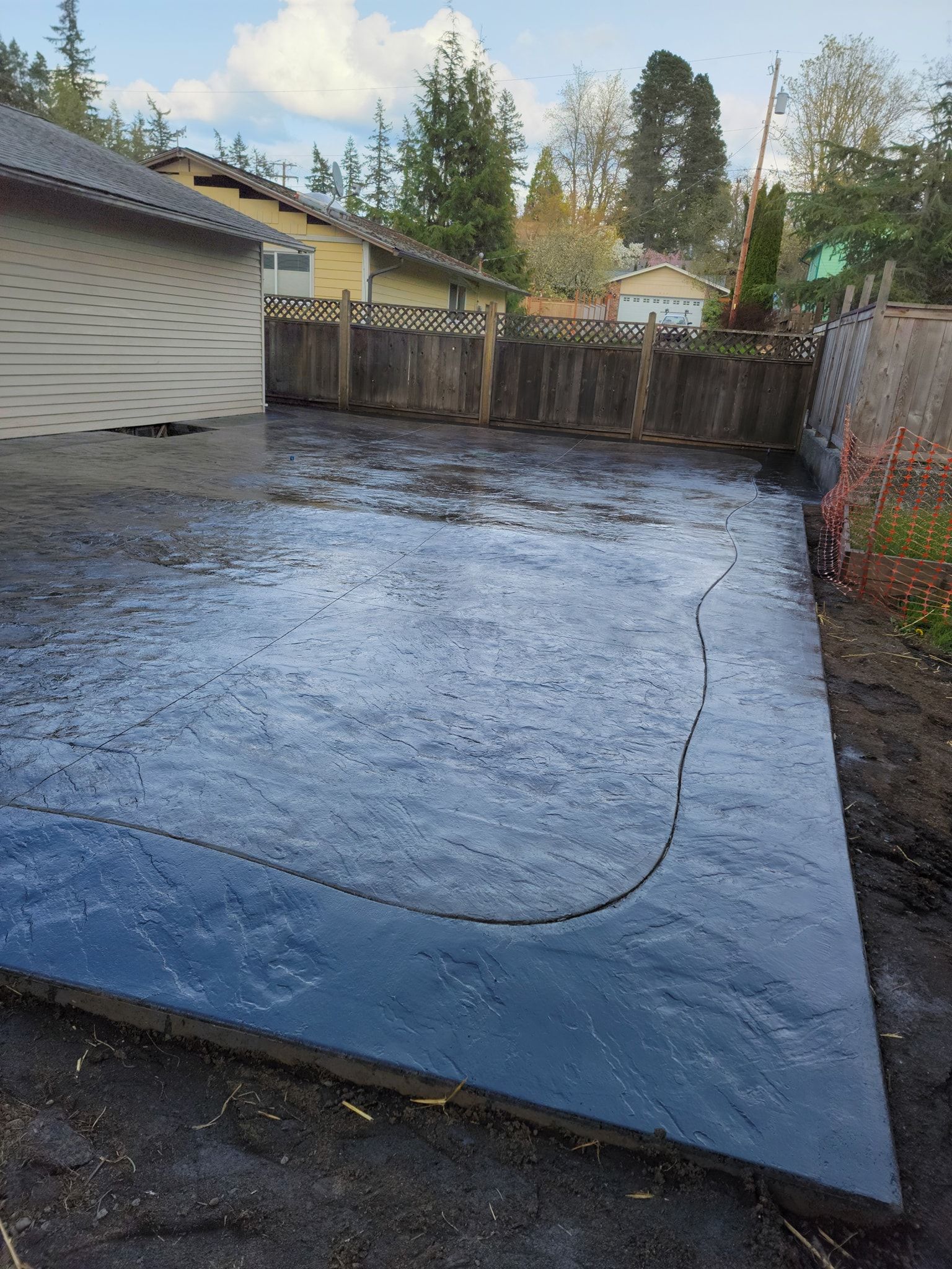 A concrete driveway with a fence and a house in the background.