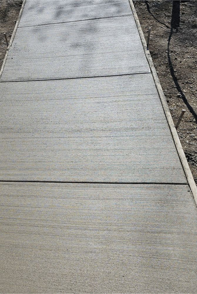 A concrete walkway going through a dirt field.