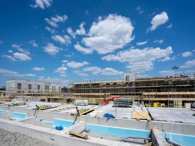Construction site with partially built structures under a blue sky with fluffy clouds.
