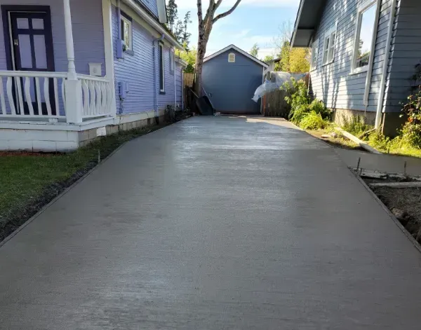 A concrete driveway between two houses with a purple house in the background.