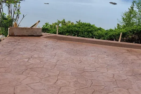 Brown stamped concrete patio with water and trees in the background.
