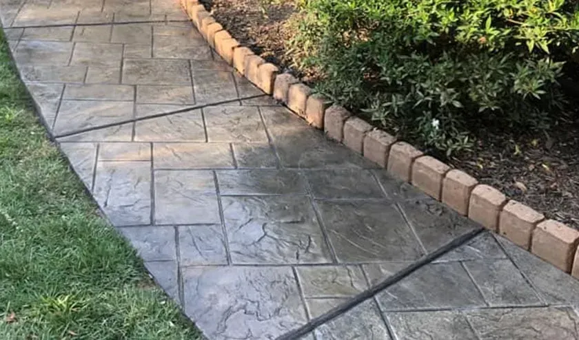 Stamped concrete walkway with brick edging and greenery on either side.