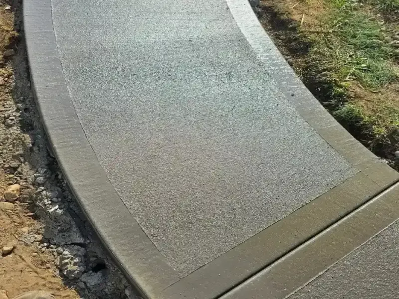 Curved concrete sidewalk with smooth gray surface beside dirt and grass edges