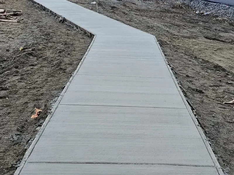 A newly poured concrete walkway curves through a dirt construction site.