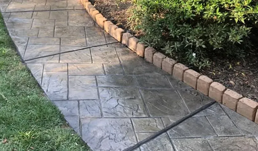 A concrete walkway leading to a garden with a brick border.