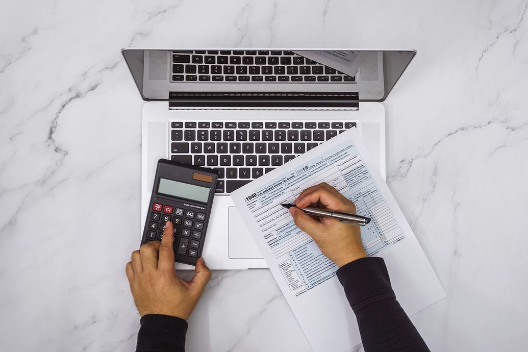 A person is using a laptop computer and a calculator while writing on a piece of paper.