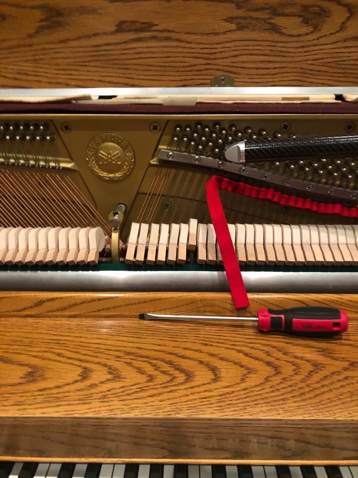 Open piano with red strap and screwdriver resting on the wooden floorboard beneath it