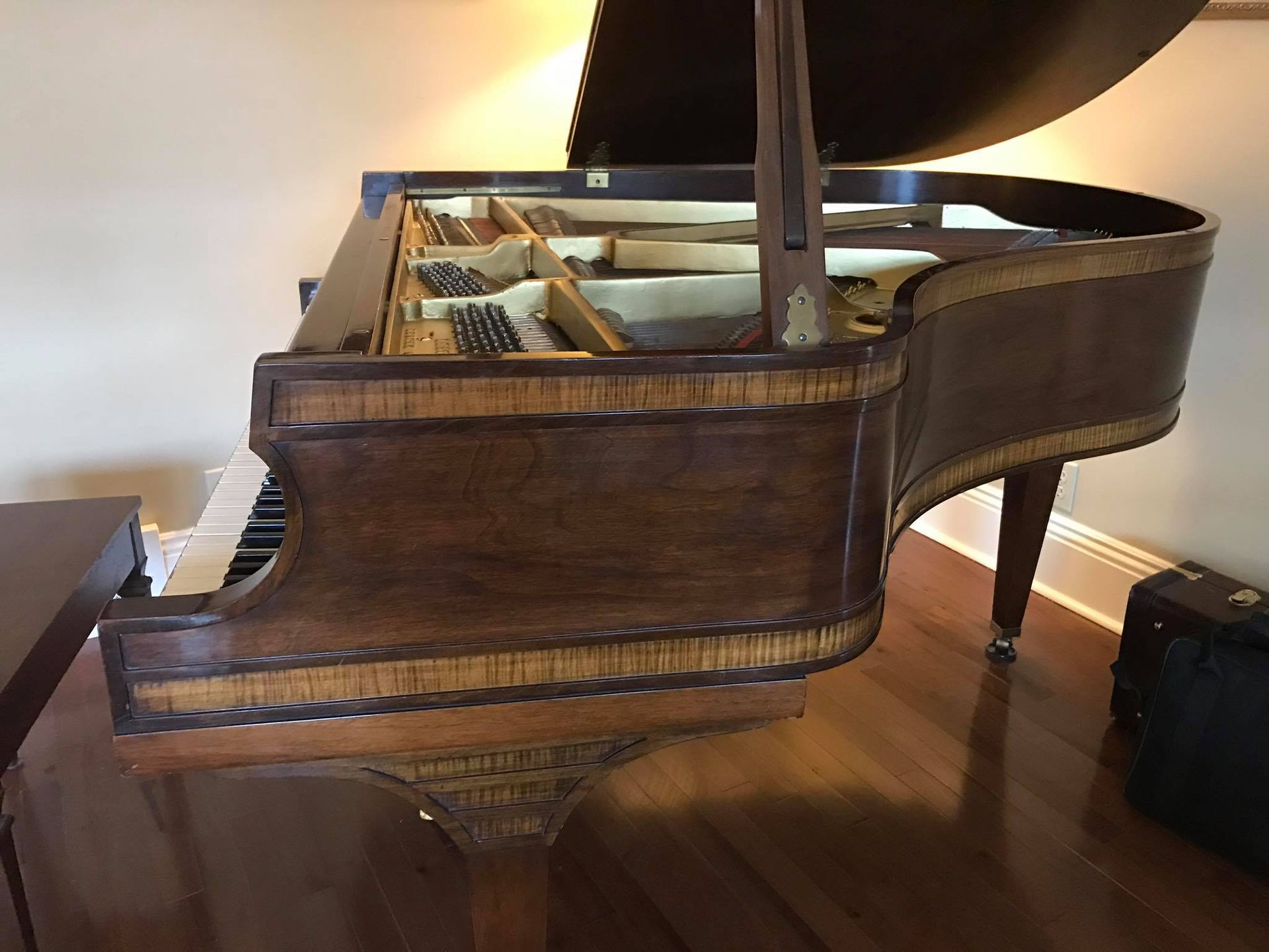 A grand piano with dark wood, featuring a light-colored ornamental wood inlay, sitting on a wooden floor.