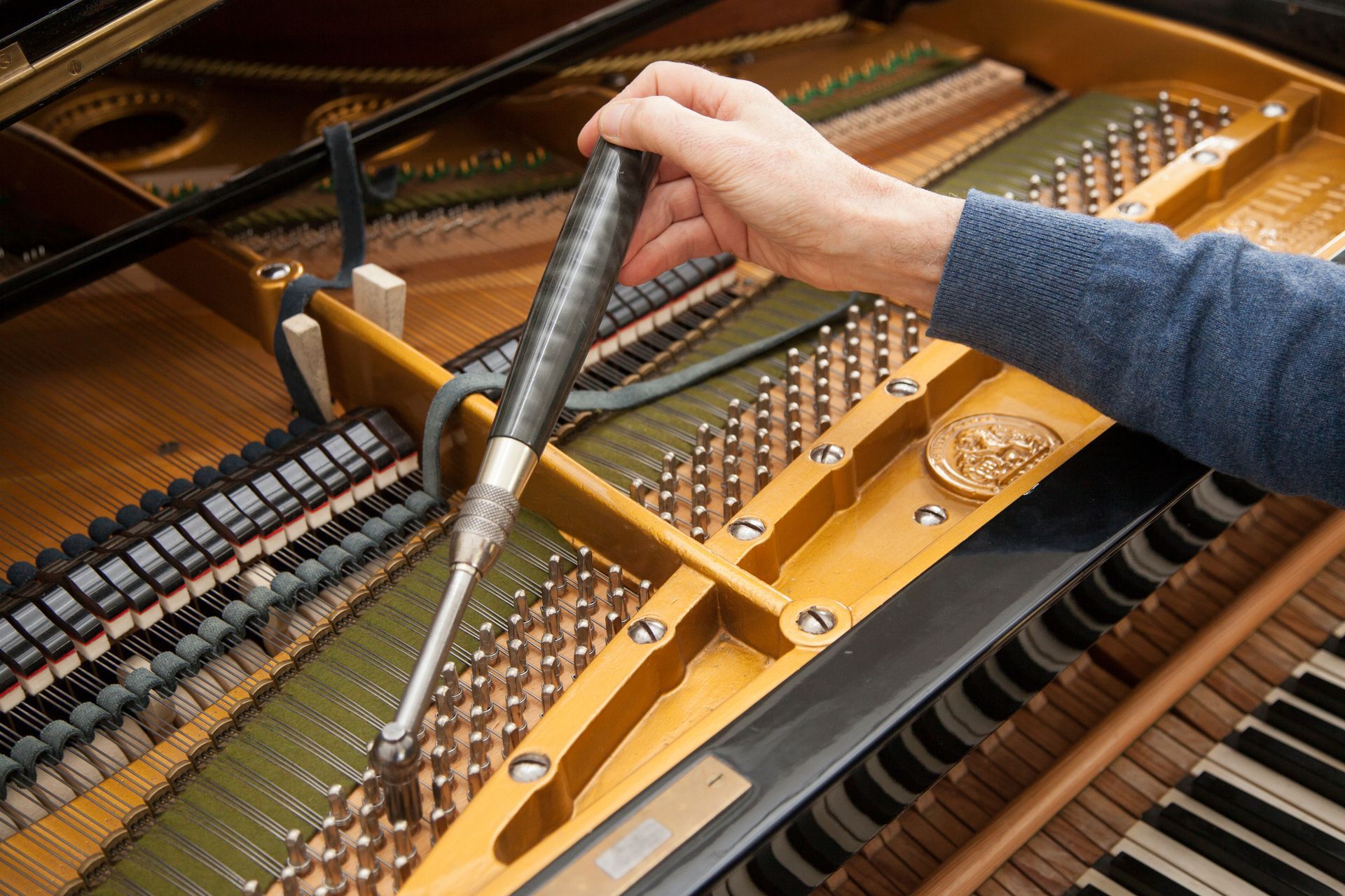 A close-up view of a person using a tuning hammer to adjust the pins inside the open case of a grand piano.