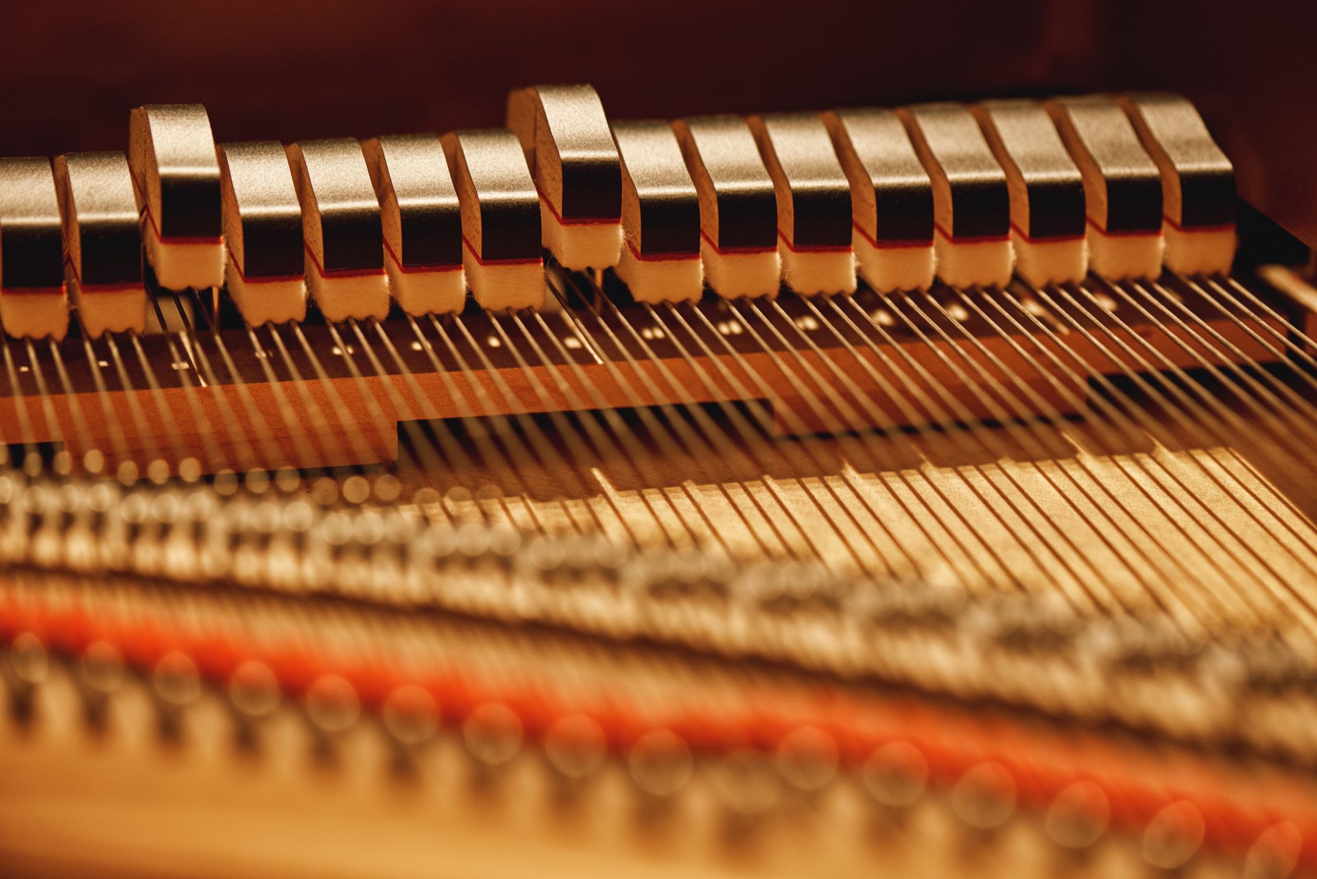 A close-up view of the interior mechanics of a grand piano, showing strings, hammers, and dampers in a warm, amber light.