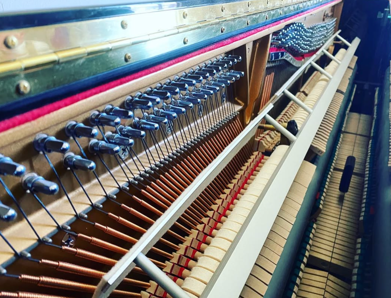 Interior view of a piano’s strings, hammers, and action mechanism in warm wood tones