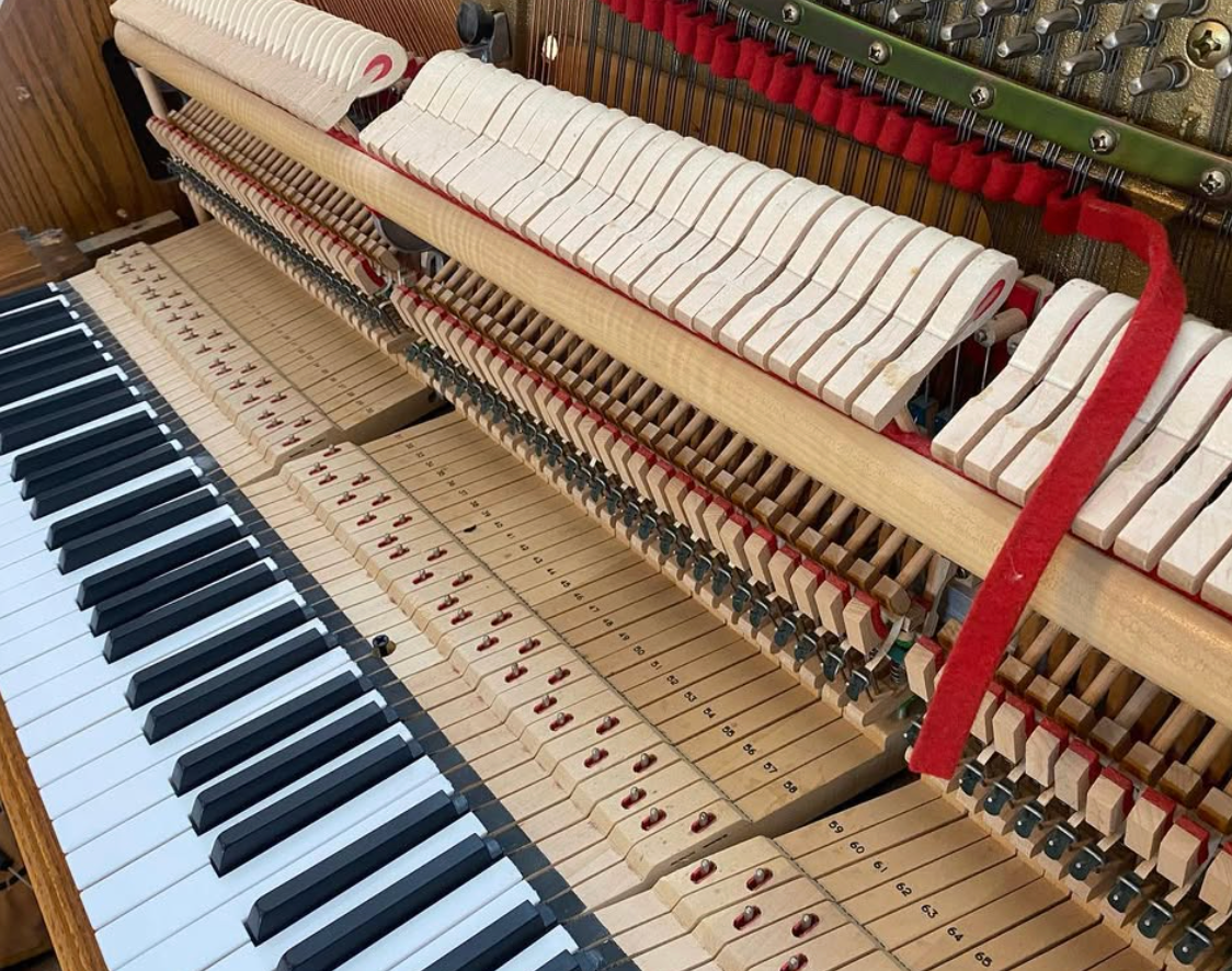 Piano keyboard and exposed internal action with strings and hammers visible inside the upright piano