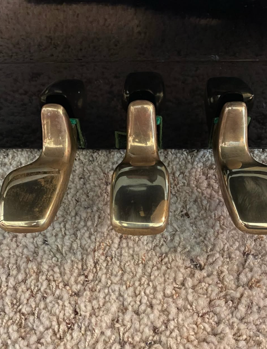 Three brass piano pedals above a beige carpet near the base of the instrument.