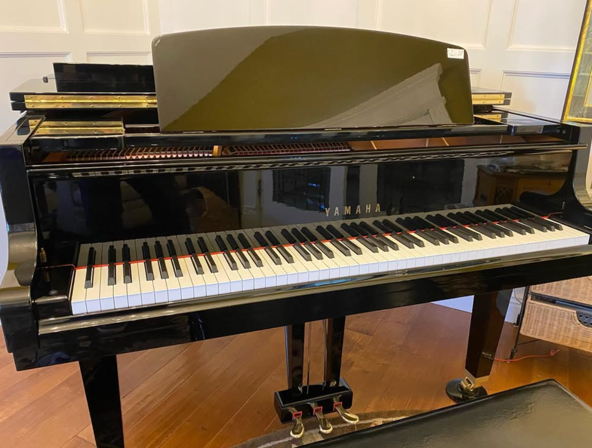 Black grand piano with lid open in a room, showing its keyboard and pedals.