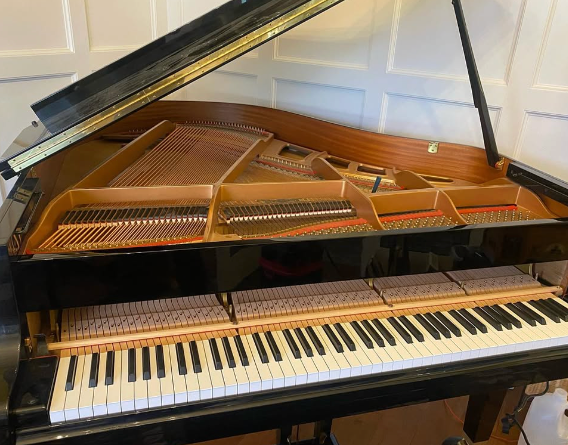 Open grand piano with lid raised, showing strings and keyboard in a room.