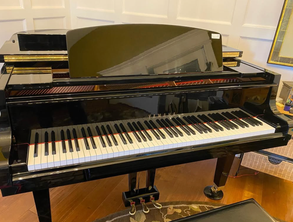 Black grand piano with open lid in a room, showing the keyboard and bench.