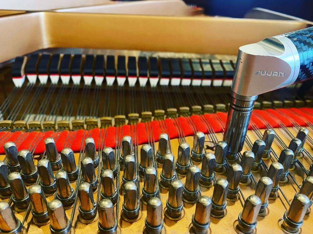 Close-up of a piano's strings and tuning pins with a tuning hammer