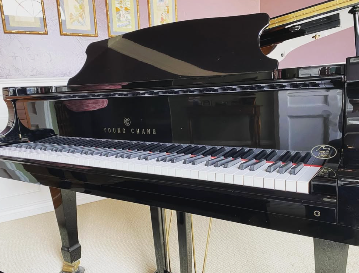 Black grand piano in a bright room, showing the keyboard and open lid