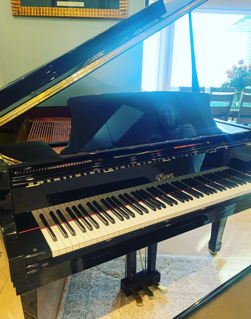 Black grand piano with raised lid in a bright room, viewed from the side