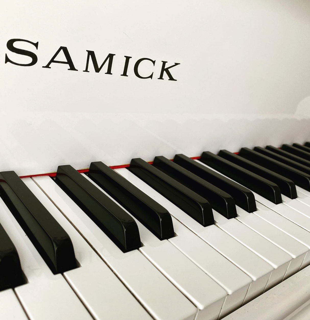 Close-up of a white Samick piano keyboard with black keys and logo on the fallboard