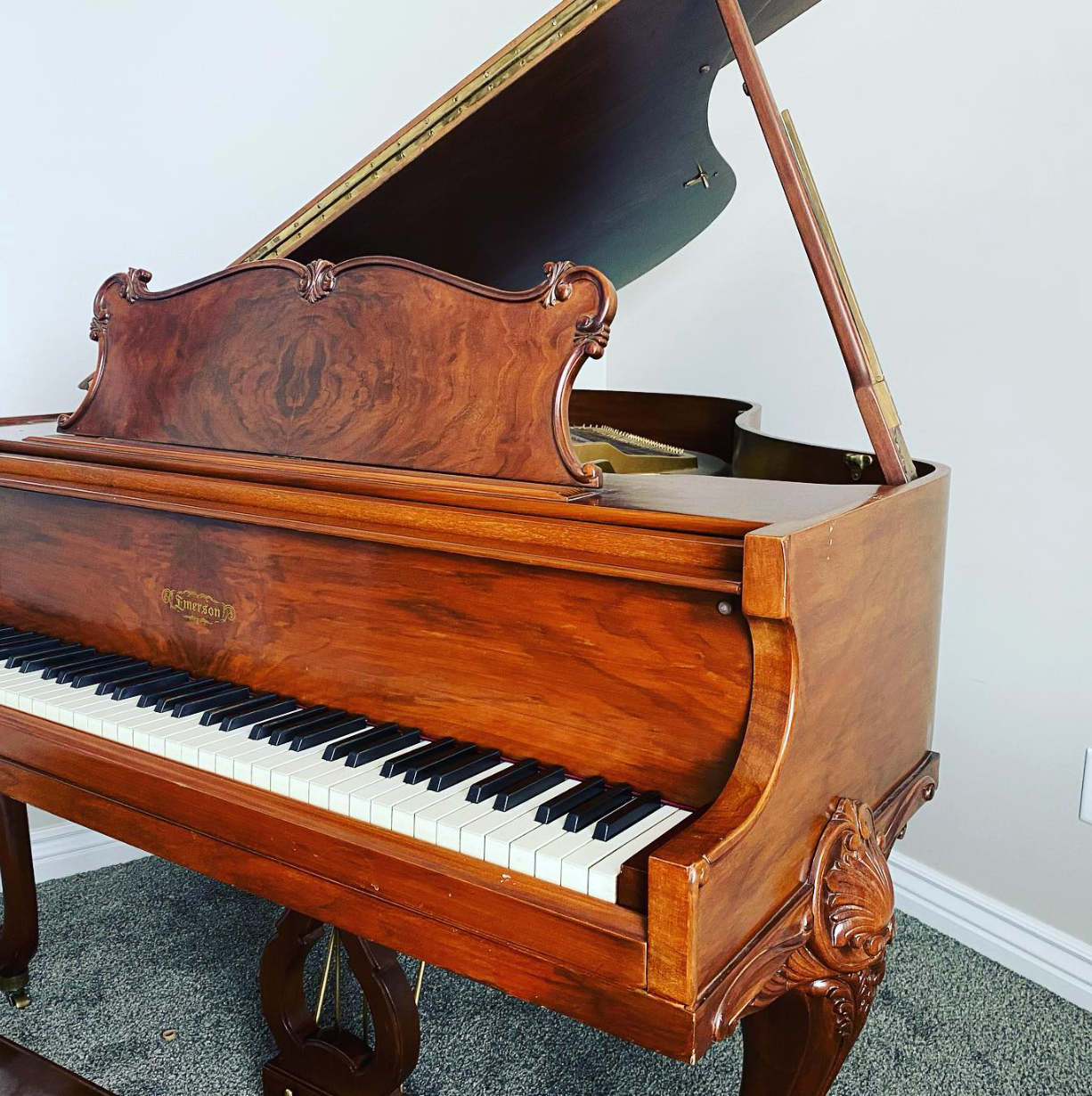Antique wooden grand piano with the lid open, shown indoors on carpet.
