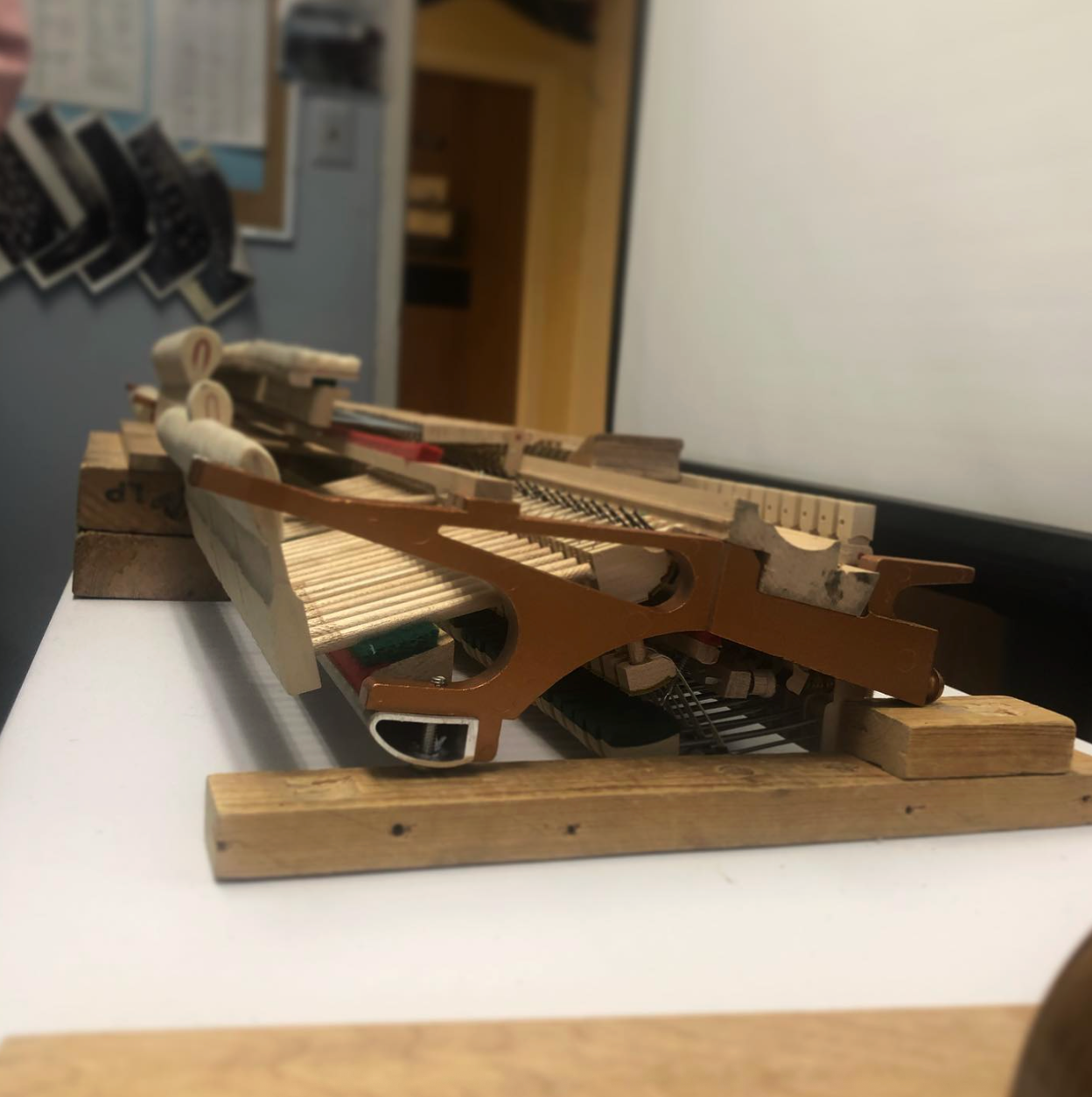 Close-up of a small wooden mechanical model on a table, with gears and levers in a workshop setting