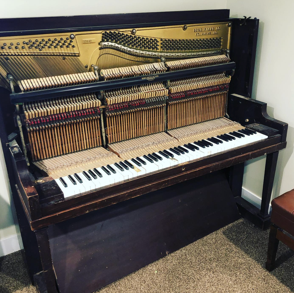 Upright piano with exposed internal hammers and strings, showing its mechanism in a room.