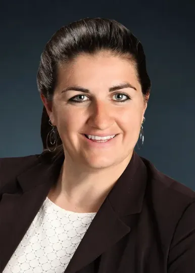 A woman in a brown jacket and white shirt is smiling for the camera.