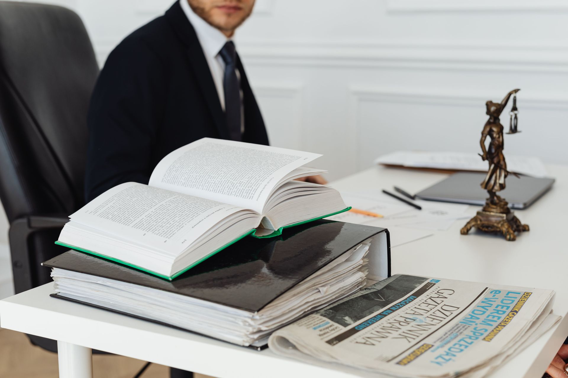 Business desk with open books, documents, and a judge figurine beside a seated man in a suit