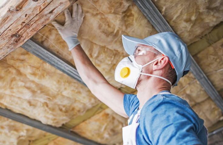 A man wearing a mask is insulating the ceiling of a house.