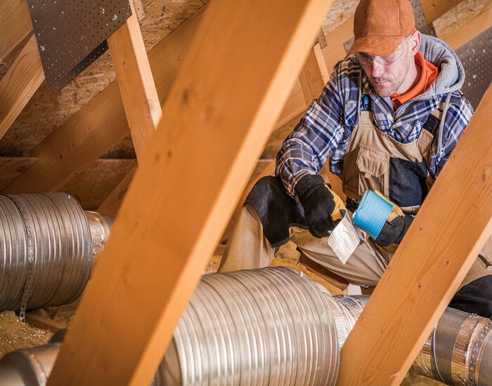 A man is working on a duct in the attic.