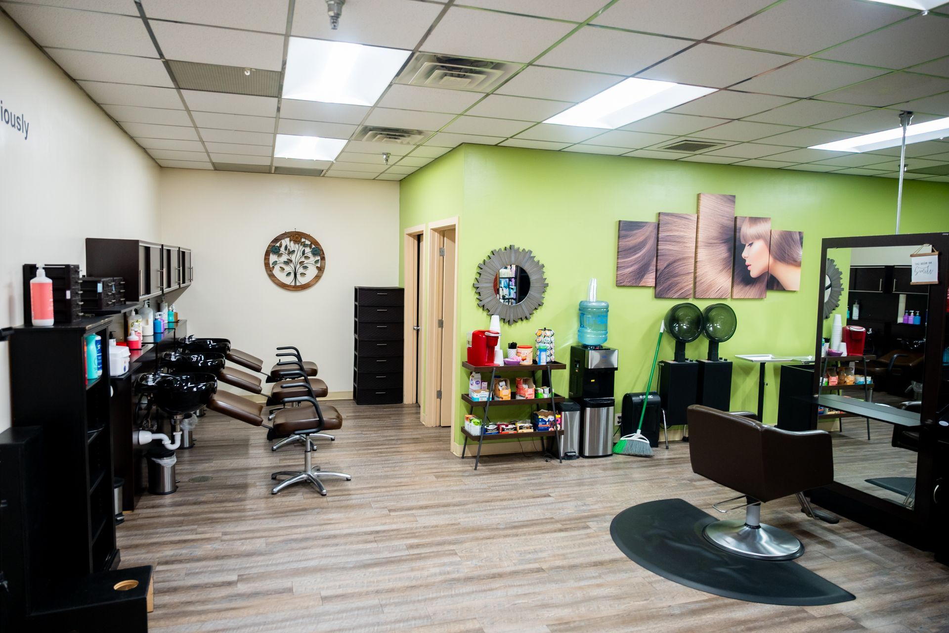 Hair salon interior with styling stations, green accent wall, and decorative art.