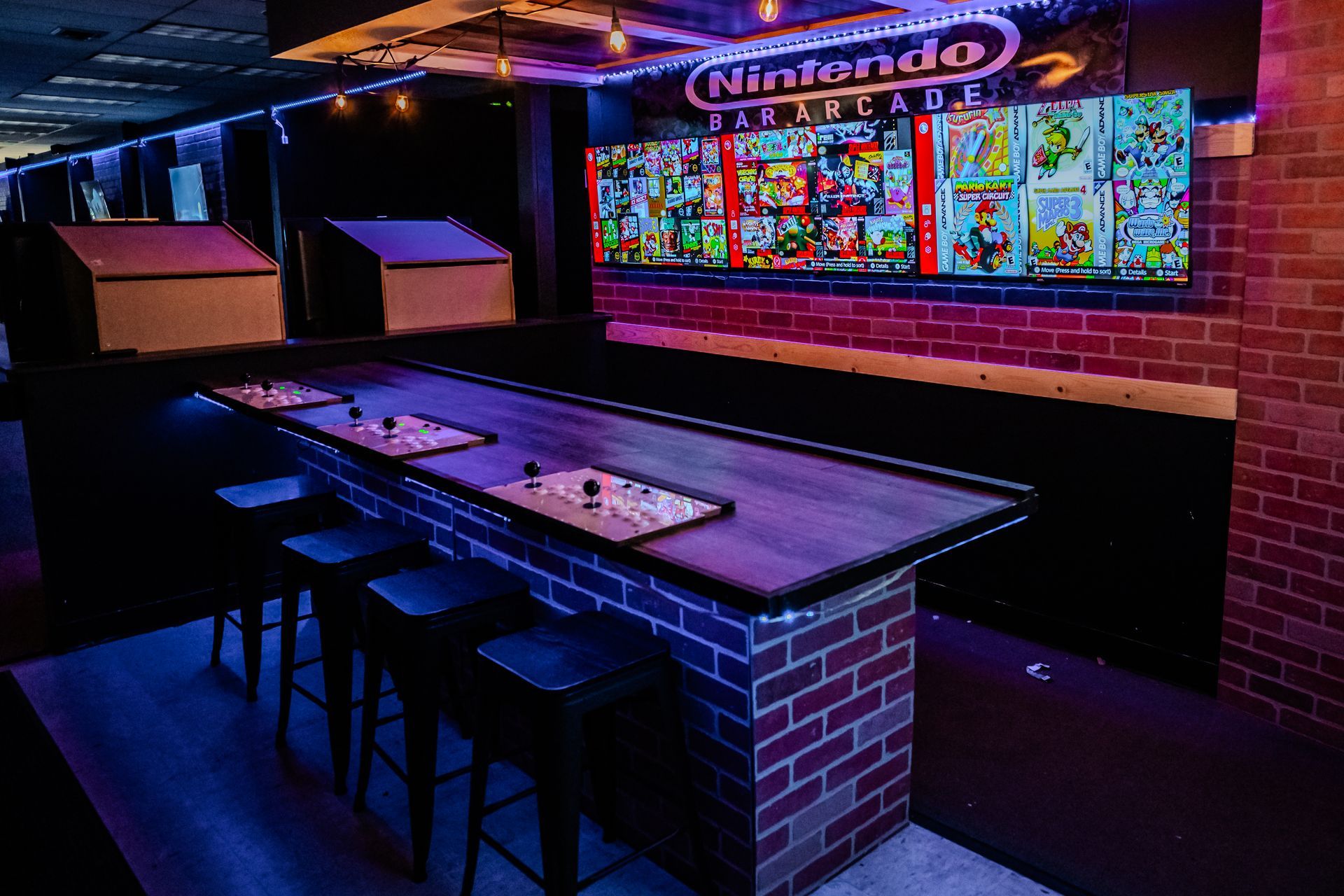 Gaming arcade with a long table, brick columns, bar stools, and Nintendo game covers on the wall.