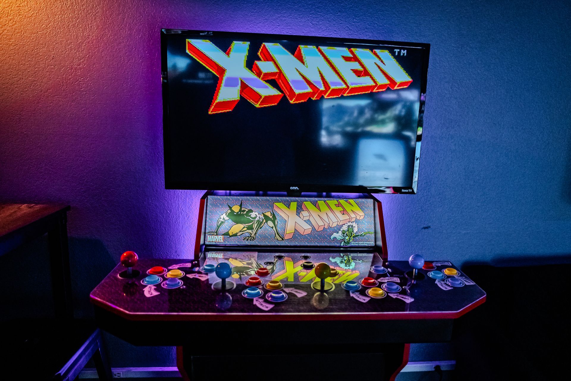 Arcade cabinet playing X-Men game, colorful joysticks and buttons. Display screen shows the game logo.