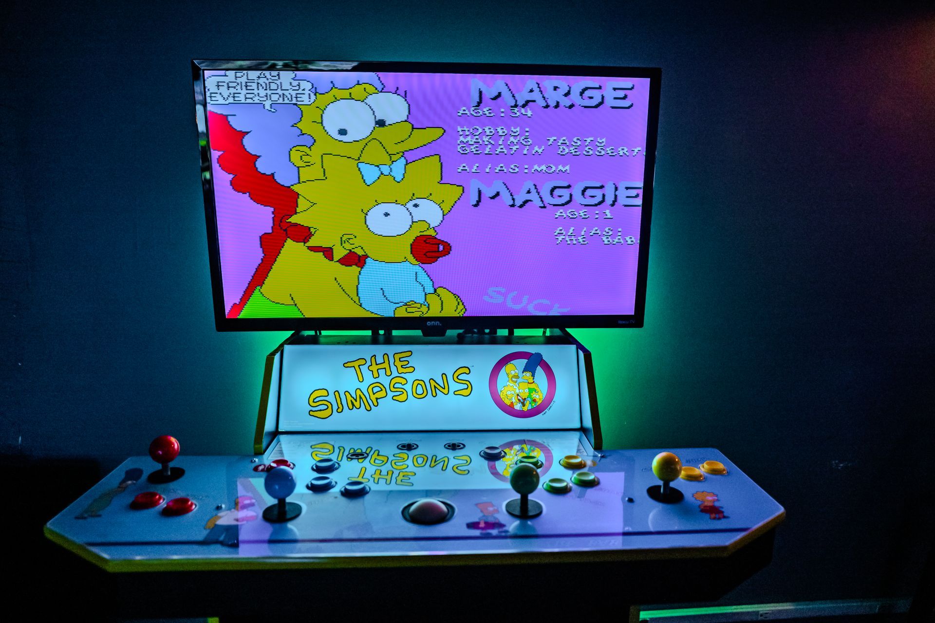 The Simpsons arcade game with a lit-up screen showing Marge and Maggie. Control panel has joysticks and buttons.