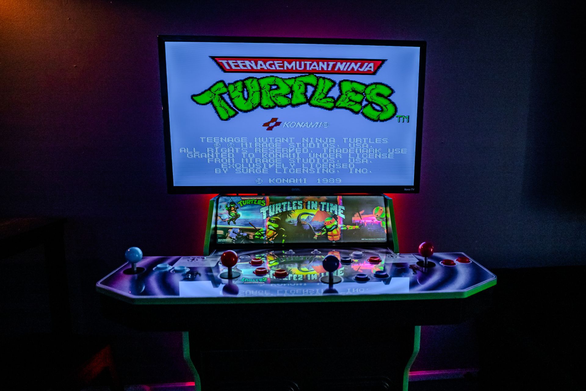 Arcade cabinet displaying Teenage Mutant Ninja Turtles game. Black, green, and red controls. Illuminated in neon.