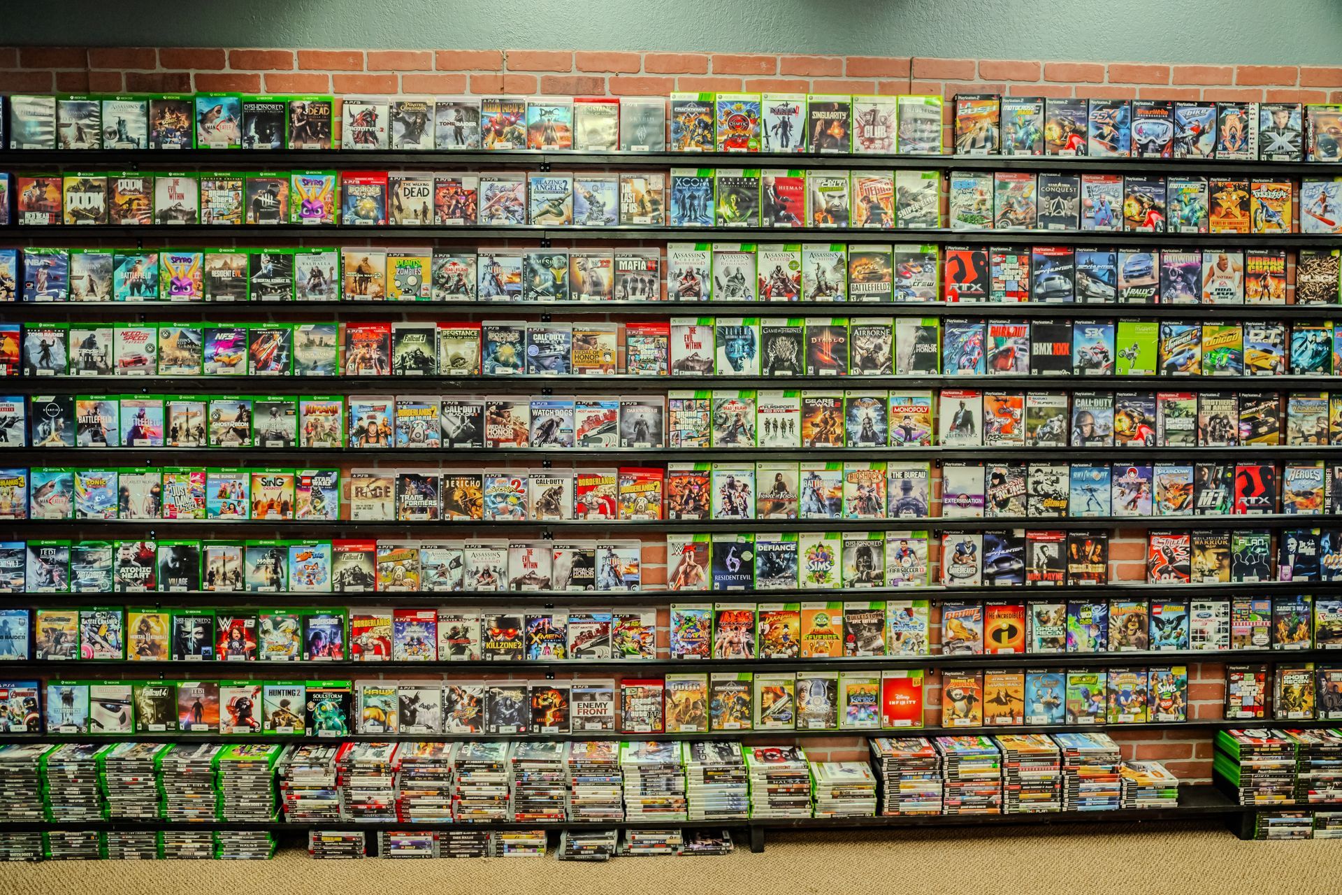 A wall filled with shelves of video game cases, organized by type, against a brick wall.