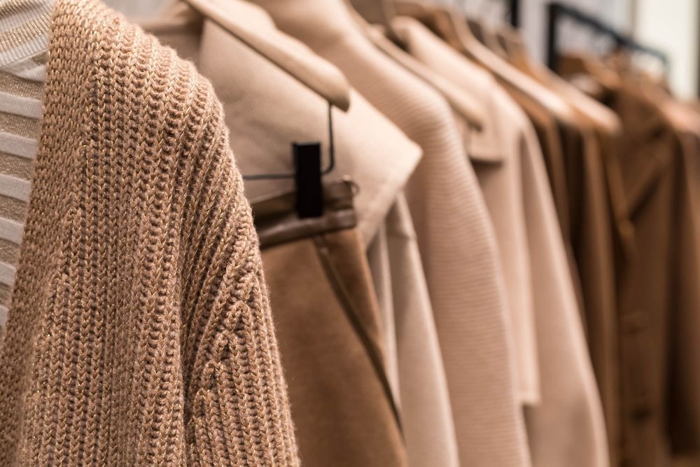 Clothes hanging on a rack in a store, including a tan sweater and coats.