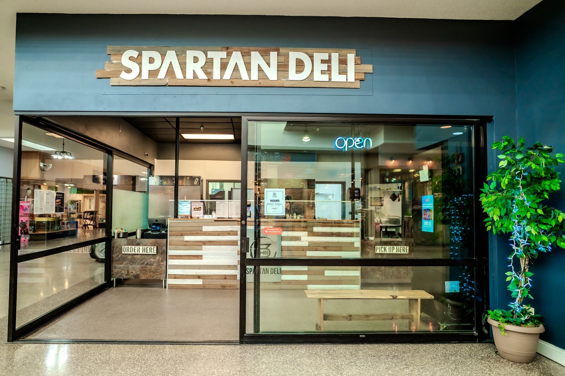 Spartan Deli storefront with glass windows and entrance, blue wall, and wooden sign.